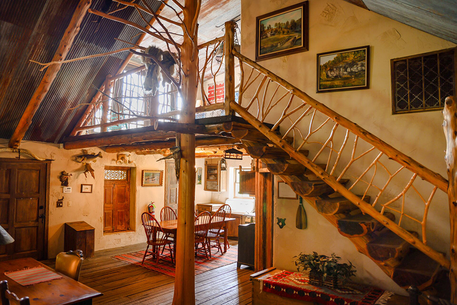 Interior photograph of a rustic hunting cabin with a wooden railing, tin roof, and historical kitchen equipment.