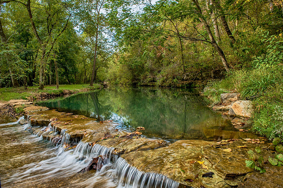 A picturesque scene of a flowing creek spilling over a rock weir within the Dogwood Canyon park.